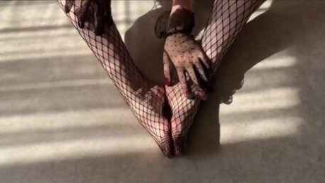 The girl caresses her legs in fishnet tights and strokes them with her hands in lace gloves